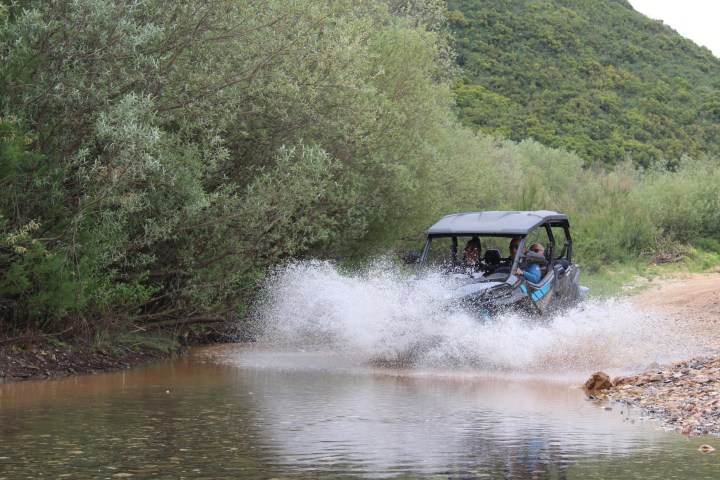 Off-road vehicle splashing through a water puddle on a dirt path with surrounding greenery.