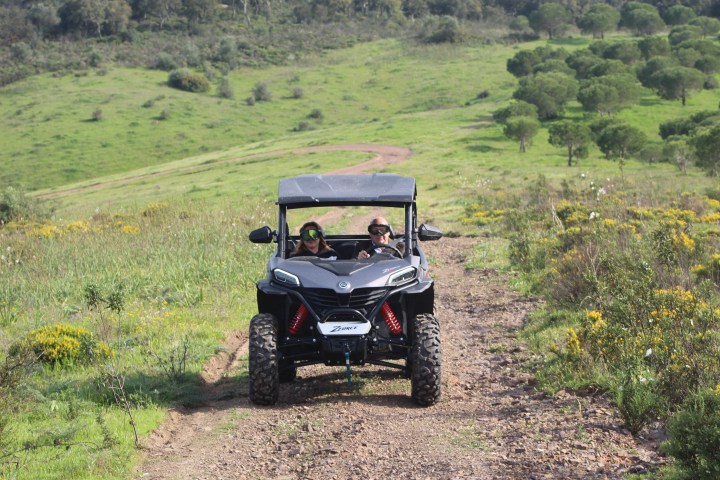 Two people on a rugged ATV ride on a dirt path through grassy terrain.